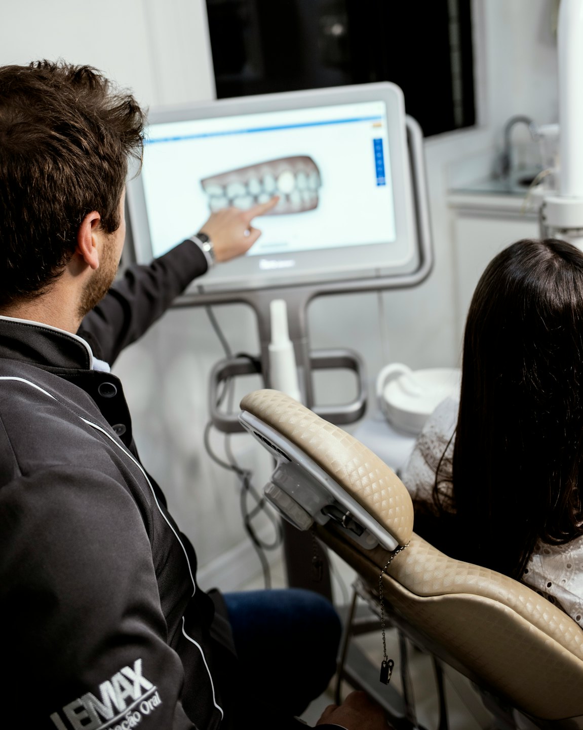 Dentist points to 3D teeth model on screen for patient.